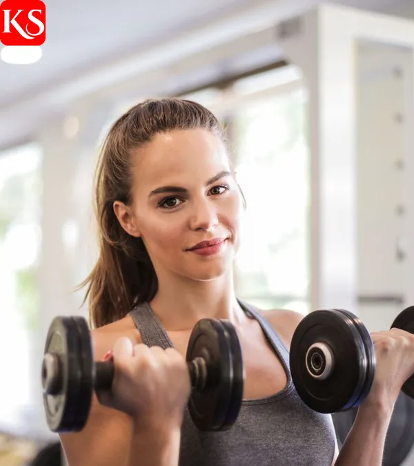 Frau trainiert nach einem Trainingsplan Muskelaufbau mit zwei Kurzhanteln im Fitnessstudio