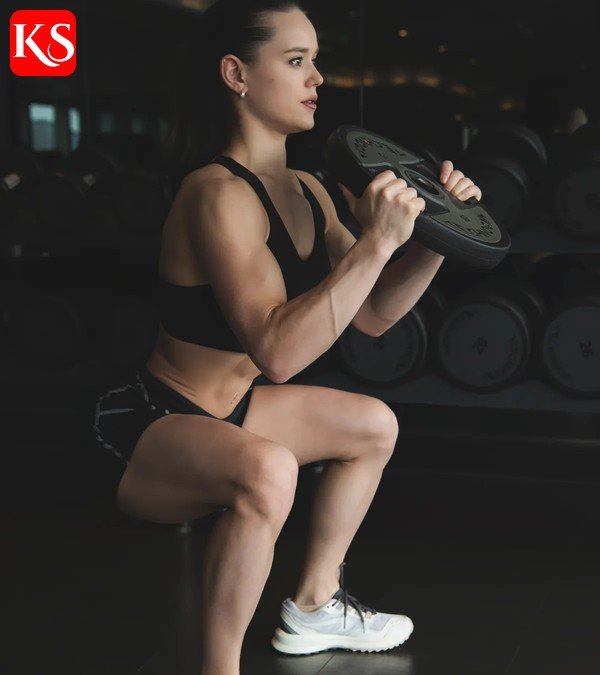 Frau macht Kniebeugen mit Kurzhantel im Fitnessstudio – Trainingsplan Fitnessstudio Frauen